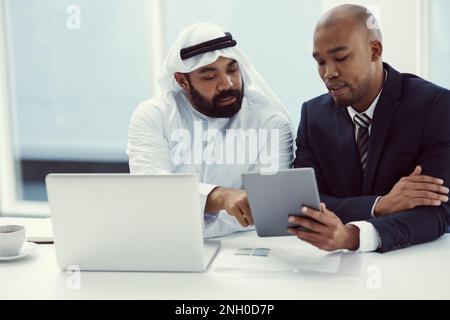 Teamwork and tech, the best tools for productivity. two businessmen using a digital tablet and laptop while having a discussion in a modern office. Stock Photo