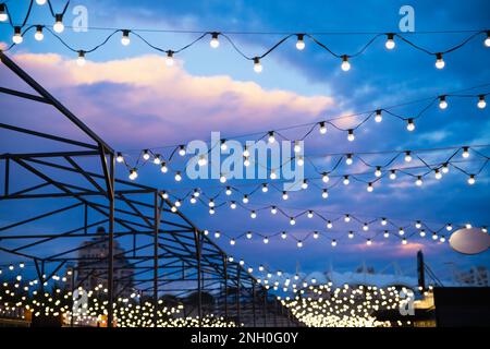 String of light bulb decorations and awning structures for outdoor activities, party, concert, festival, fun fair. Street outside lighted light bulbs Stock Photo