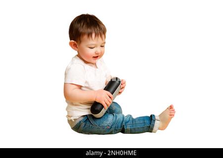 Toddler baby plays with a wireless music speaker on a studio isolated on a white background. Happy child in a white t-shirt listens to music in an aud Stock Photo