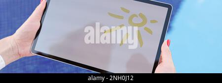 Female hands hold tablet with drawn sun and white screen above pool Stock Photo