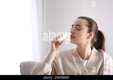 Sick young woman using nasal spray at home Stock Photo