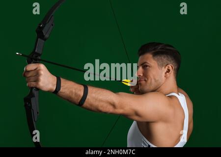Man with bow and arrow practicing archery on green background Stock Photo
