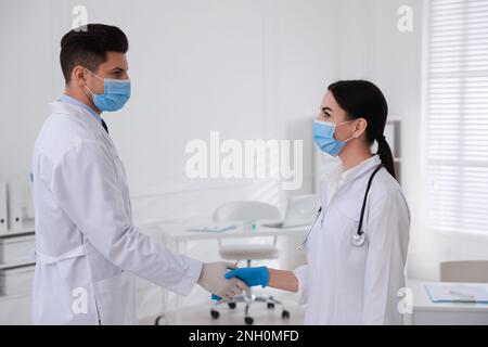 Doctors in medical gloves with protective masks giving handshake at hospital Stock Photo