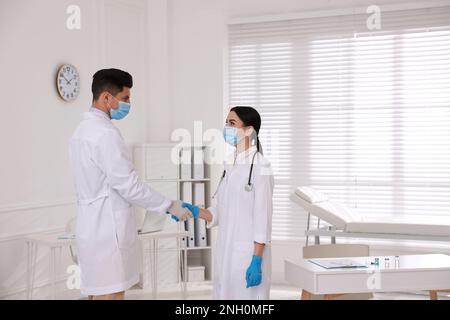 Doctors in medical gloves with protective masks giving handshake at hospital Stock Photo