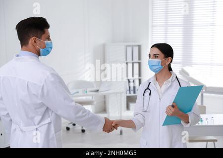 Doctors with protective masks giving handshake in clinic Stock Photo