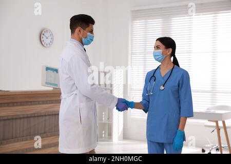 Doctors in medical gloves with protective masks giving handshake at hospital Stock Photo
