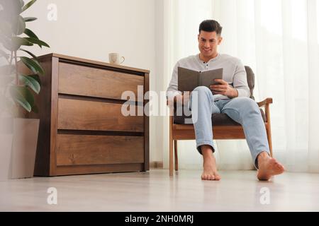 Man with book sitting in armchair at home. Floor heating system Stock Photo