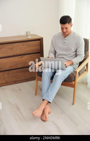 Man with laptop sitting in armchair at home. Floor heating system Stock Photo