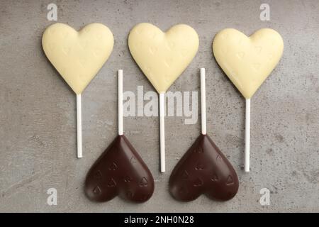 Different chocolate heart shaped lollipops on grey table, flat lay Stock Photo