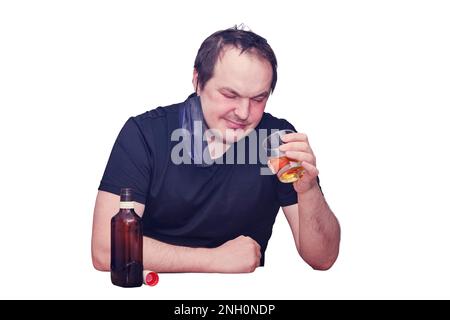 A man looks thoughtfully at a glass of whiskey sitting in a home kitchen, isolated on a white background. Problems with drinking alcohol during a pand Stock Photo