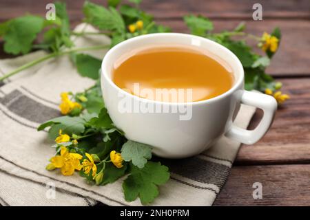 Cup of aromatic celandine tea and flowers on wooden table, closeup Stock Photo