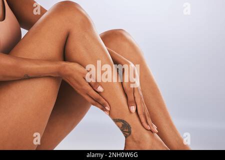 Hands, legs and beauty with a black woman in studio, sitting on the floor against a gray background for skincare. Fitness, body and tattoo with a Stock Photo