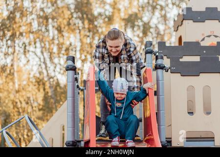 A boy, person with down syndrome walks in the park with his mother, going down the children's slide Stock Photo