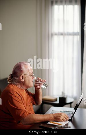 Senior man drinking glass of water after fishing working on laptop Stock Photo