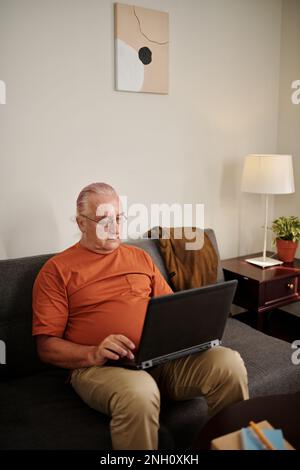 Senior man sitting on couch and working on laptop Stock Photo