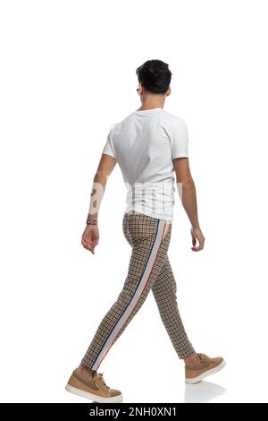 side and back view of casual guy looking away and walking in front of white background in studio Stock Photo