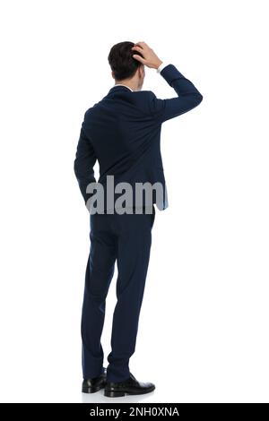 elegant businessman scratching his head and feeling confused, wearing a suit and tie against white background Stock Photo