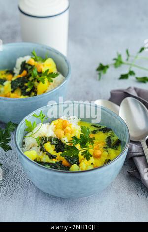Vegan chickpea potato curry with rice and kale in blue bowl, gray background. Alternative plant-based eco friendly food concept. Stock Photo
