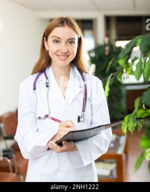Young positive female therapist writes notes on a tablet, standing in the lobby Stock Photo