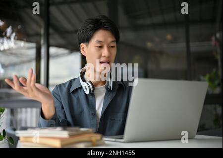 Concentrated and professional young Asian businessman or freelance programmer remote working at the cafe, using laptop, having an online meeting with Stock Photo