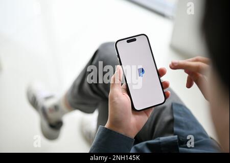 Chiang Mai, Thailand - Feb 17 2023: close-up image of an Asian man using PayPal mobile application to pay his bills. iPhone with PayPal logo on screen Stock Photo
