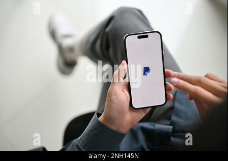 Chiang Mai, Thailand - Feb 17 2023: close-up image of an Asian man using PayPal mobile application to pay his bills. iPhone with PayPal logo on screen Stock Photo
