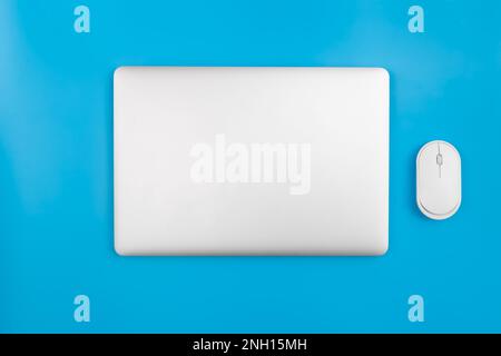 Closed laptop and computer mouse on a blue background, top view. Stock Photo