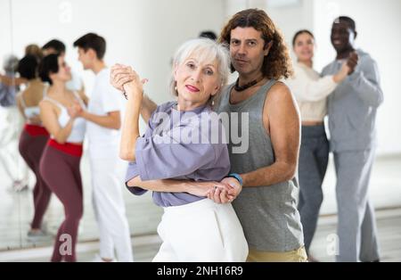 Happy caucasian guy and old lady practising paired latin dance in dance studio Stock Photo
