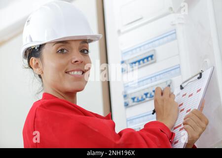 happy female builder inspecting fuse board Stock Photo