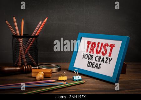 Trust Your Crazy Ideas. Motivational quote. Picture frame on the office table. Stock Photo