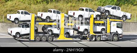 Seven Isuzu white pickup trucks loaded onto flexible adjustable car vehicle transporter trailer towed by hgv lorry truck driving on UK motorway road Stock Photo