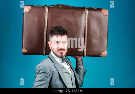 heavy bag. mature traveller. bearded man in formal suit. stylish esthete with vintage bag. businessman in bow tie. business trip with retro suitcase Stock Photo