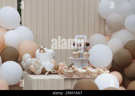 Creative gender neutral baby shower or birthday decoration in the garden. Bohemian style outdoor event set up with balloons. White cream peach caramel Stock Photo