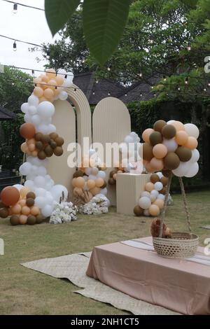 Creative gender neutral baby shower or birthday decoration in the garden. Bohemian style outdoor event set up with balloons. White cream peach caramel Stock Photo