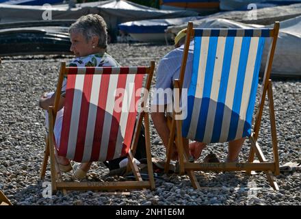 older couple seated in deck chairs on stony beach beer devon england Stock Photo