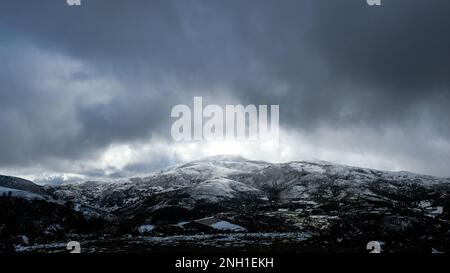 An idyllic snow-capped mountain against a dramatic dark sky, punctuated by illuminated clouds Stock Photo