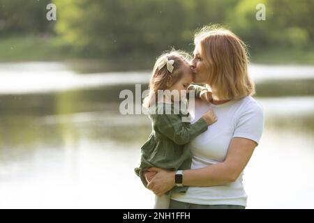 Mom holds her daughter and kisses her forehead Stock Photo