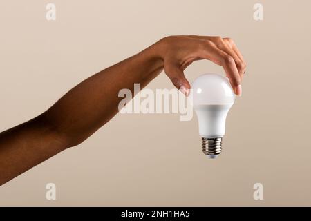 Crop anonymous African American female hand demonstrating modern LED light bulb against beige background Stock Photo