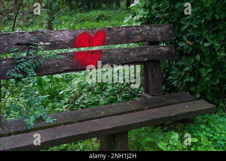 Bright red heart painted on the back of a wooden bench in the park Stock Photo