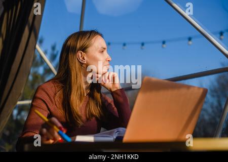 Young thoughtful girl makes notes in a notebook. Woman illuminated by the warm light of sunset. Stock Photo