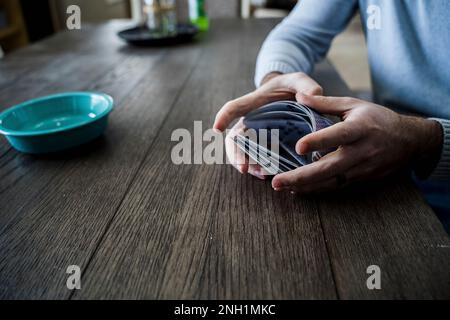 Caucasian Man Shuffling a Deck of Playing Cards at Dining Table Stock Photo
