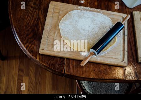 Black Rolling Pin Set on Pasta Dough on Wooden Cutting Board Stock Photo