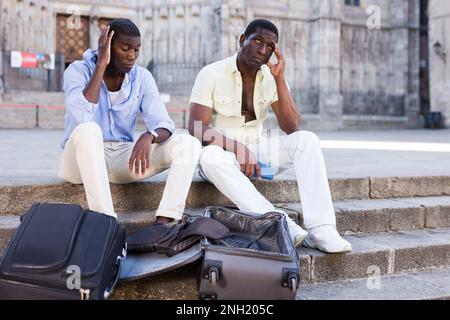 Two frustrated african american travelers sitting with empty suitcases Stock Photo