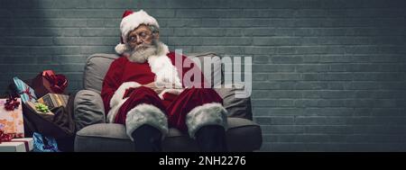 Sleepy Santa Claus taking a nap and relaxing on the armchair on Christmas Eve Stock Photo