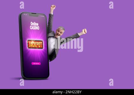 Big smartphone with online casino games interface on screen and cheerful winning man celebrating his victory, copy space Stock Photo