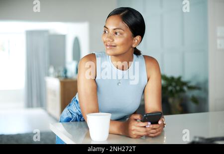 Thinking of the best title for my blog post. an attractive young woman leaning on her kitchen counter and looking contemplative while using her Stock Photo