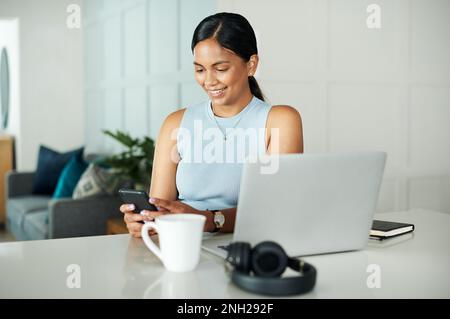 This is such a funny text. an attractive young woman sitting alone at her kitchen counter and using her cellphone. Stock Photo