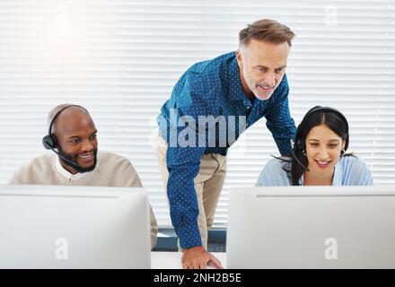 Are you doing alright. two call centre agents sitting in the office and using their computers while getting help from their manager. Stock Photo