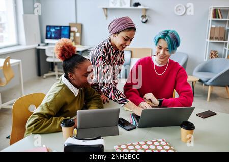 Diverse group of creative young people using laptop during meeting in office and smiling cheerfully Stock Photo