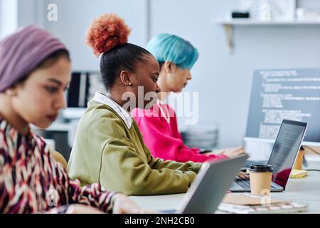 Diverse group of creative young people sitting in row while working in office focus on black young woman using laptop Stock Photo